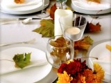 a modern organic wedding tablescape with white linens, bold leaves on the table and place settings and candles is a lovely and easy to realize idea