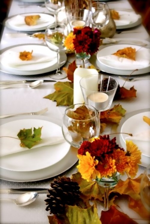 a modern organic wedding tablescape with white linens, bold leaves on the table and place settings and candles is a lovely and easy to realize idea