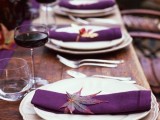 a bright fall wedding table setting with an uncovered table, purple napkins, a purple table runner and bright fall leaves is amazing