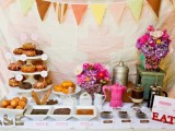 a colorful rustic donut bar with a bright bunting, bright blooms, donuts and various dips and toppings
