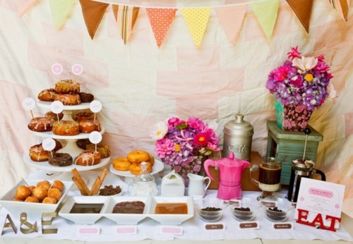 a colorful rustic donut bar with a bright bunting, bright blooms, donuts and various dips and toppings