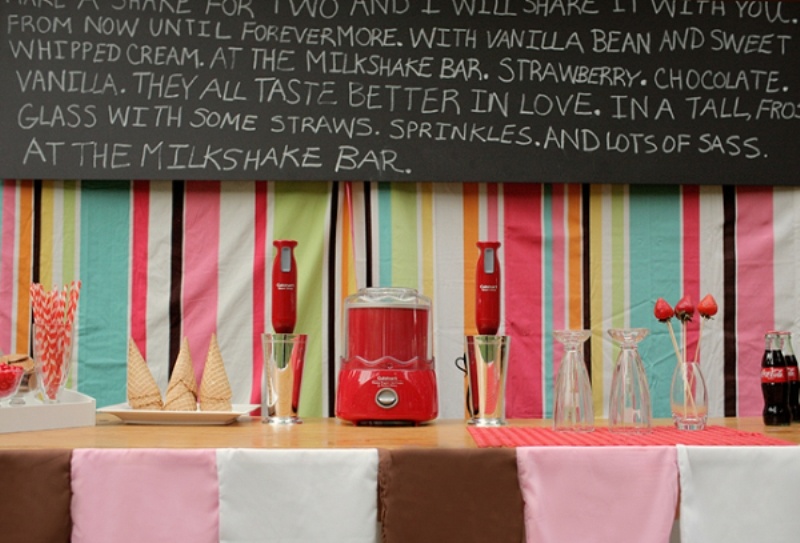 A colorful retro ice cream bar with a bright striped backdrop, strawberries, cones and an oversized chalkboard sign