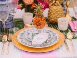a bright and colorful wedding tablescape with a green printed runner with lots of fruit and candles, gold chargers and cutlery and a colorful floral centerpiece