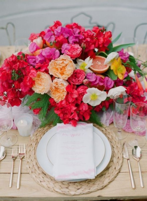 a bold tropical wedding tablescape in neutrals, with a woven charger and a bold floral centerpiece with citrus and fruits