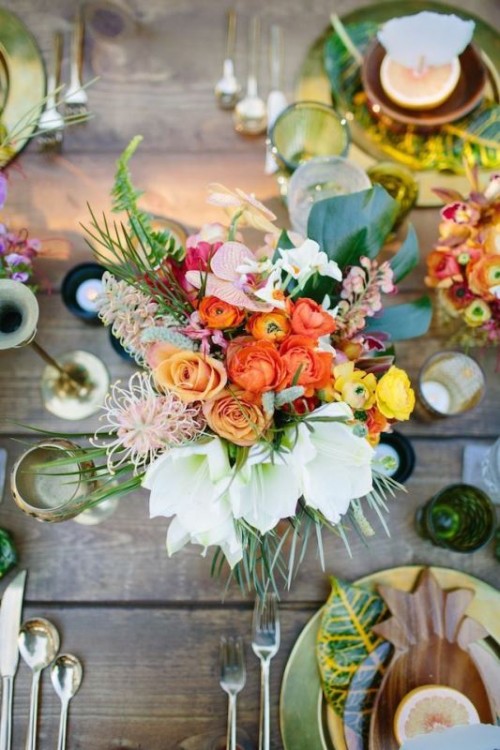 a colorful tropical wedding tablescape with a super bold floral centerpiece and tropical leaves, candles and colored glasses