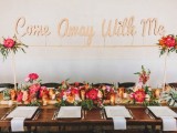 a bright tropical wedding tablescape with pink and red blooms and greenery, candles, succulents, air plants and some floral arrangements over the table