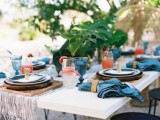 a simple yet bright wedding tablescape with a neutral table runner, blue napkins, blue glasses and bold cocktails