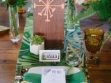 a bold tropical wedding tablescape with a bold tropical table runner, green napkins and tropical leaves for decor, colorful glasses