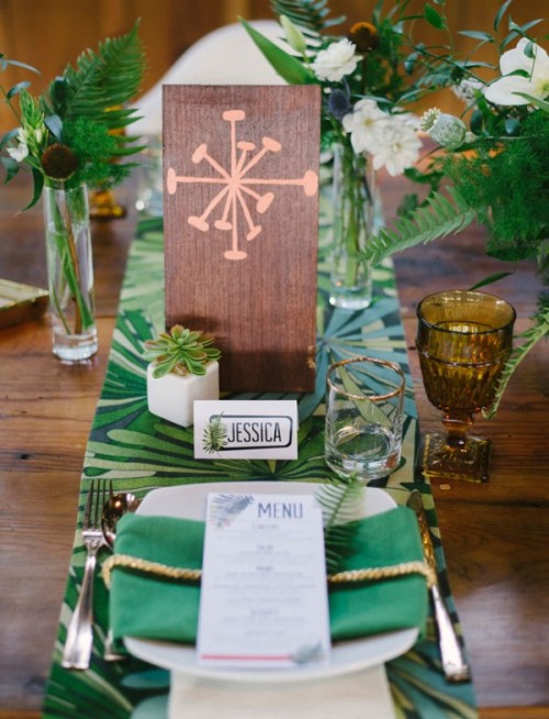 a bold tropical wedding tablescape with a bold tropical table runner, green napkins and tropical leaves for decor, colorful glasses