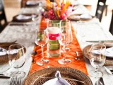 a bold wedding tablescape in neutrals and orange, with woven chargers, bright blooms and simple cutlery
