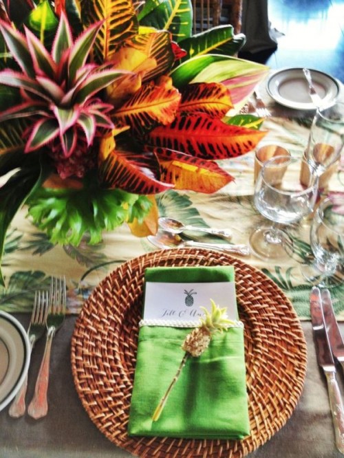 a bold wedding tablescape with a tropical tablecloth and napkins, bold leaves, woven chargers and cutlery