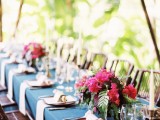 a bright tropical wedding tablescape with a navy tablecloth, blush napkins, super bold floral arrangements and candles