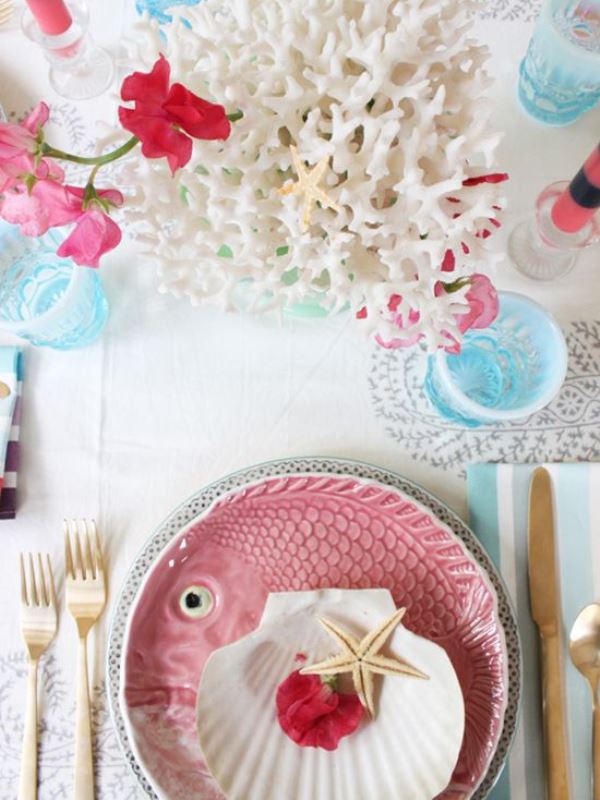 A creative tropical beach wedding tablescape with pink and blue touches, corals, starfish, a pink fish plate and blooms and blue goblets
