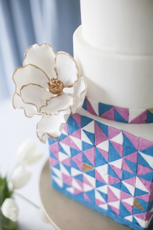 a round and square wedding cake with colorful triangles and a large white sugar bloom on the side is a lovely and bold idea for a modern and colorful wedding