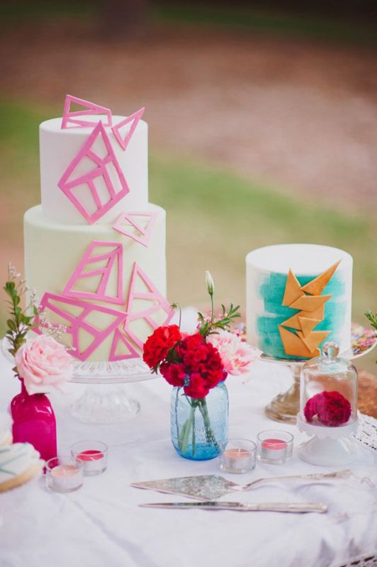 A gorgeous wedding cake with hot pink sugar shards that cover it and a white wedding cake with turquoise brushstrokes and gold triangles covering it is a lovely idea