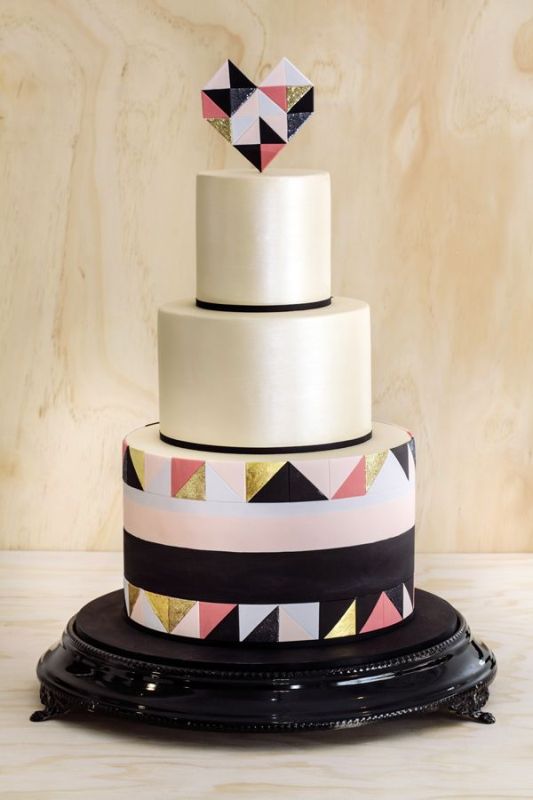 a round wedding cake with black lines, with a bold pink, gold and black triangle tier and a matching geometric heart topper is pure fun and chic