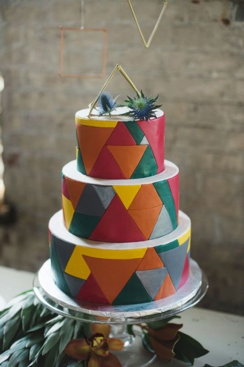 a colorful round wedding cake with bright triangles all over the cake, with a himmeli topper and thistles on top is a bright and fun idea for a wedding