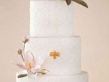 a white round wedding cake covered with hexagon patterns and with a couple of large sugar blooms looks refined and modern