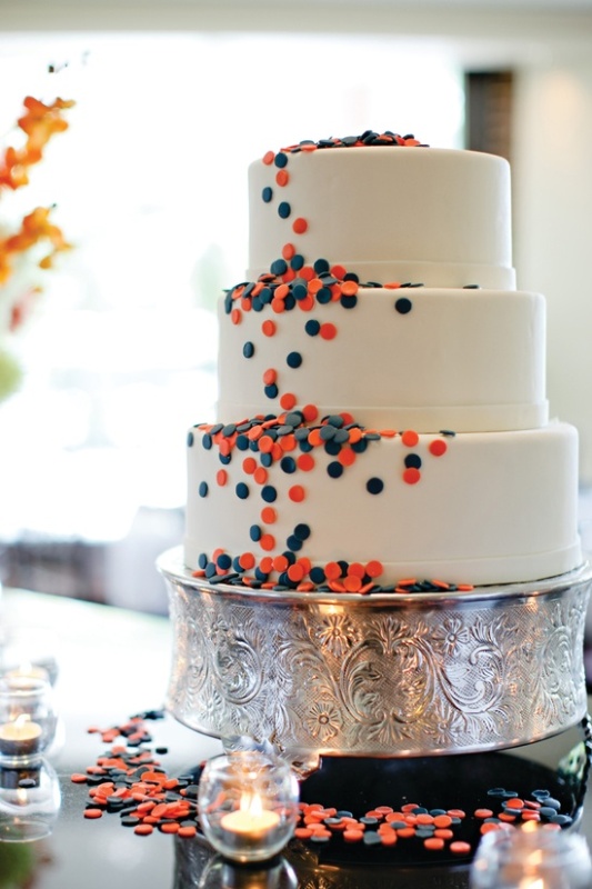 A white wedding cake with navy and coral piink polka dots for decor is an unobtrusive way to rock the color scheme