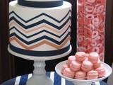 a geometric white wedding cake with navy and coral chevrons and coral blooms on top plus coral macarons next to it