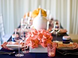 a bold navy and coral table setting with coral blooms and candle holders, a navy tablecloth and prints
