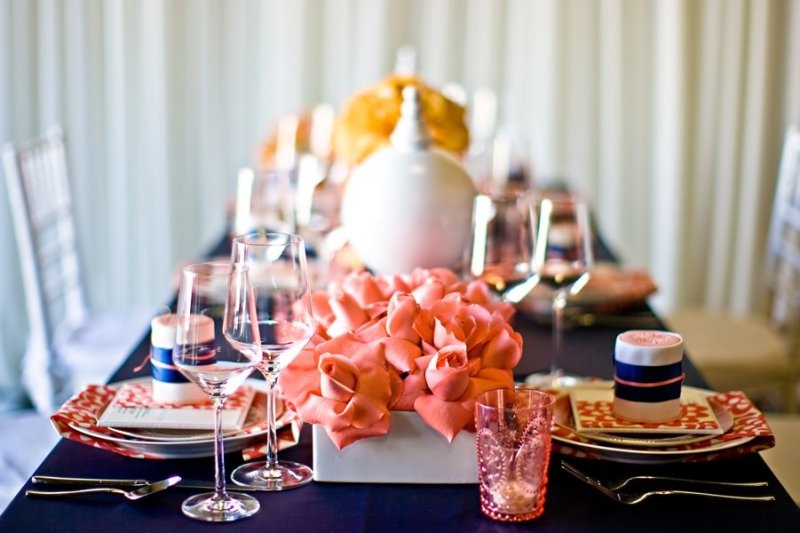 A bold navy and coral table setting with coral blooms and candle holders, a navy tablecloth and prints