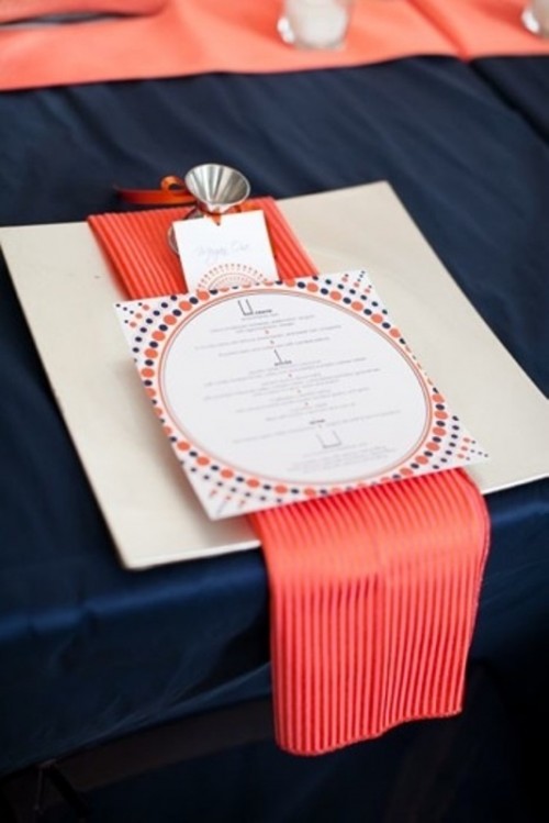 a navy tabecloth, a large charger, a striped coral napkin and a printed menu for a bold place setting