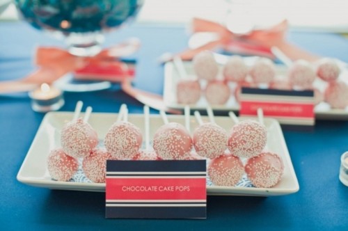a sweets table decorated with a navy tabecloth, a navy and coral card and coral pink cake pops
