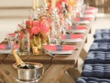 a rustic tretle table with coral blooms and a coral napkin with a navy napkin ring and a wodoen bench with tufted navy cushions