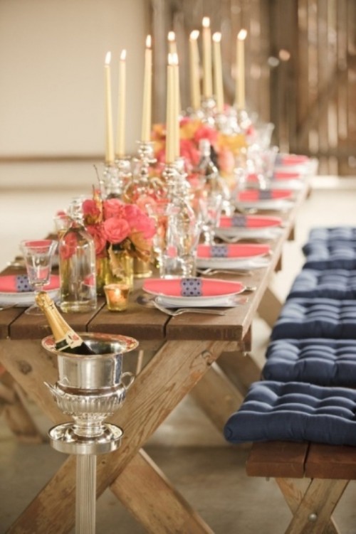 a rustic tretle table with coral blooms and a coral napkin with a navy napkin ring and a wodoen bench with tufted navy cushions