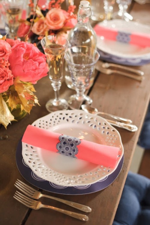 coral napkins with blue napkin rings and coral blooms and navy chargers plus gold accents to highlight the table setting