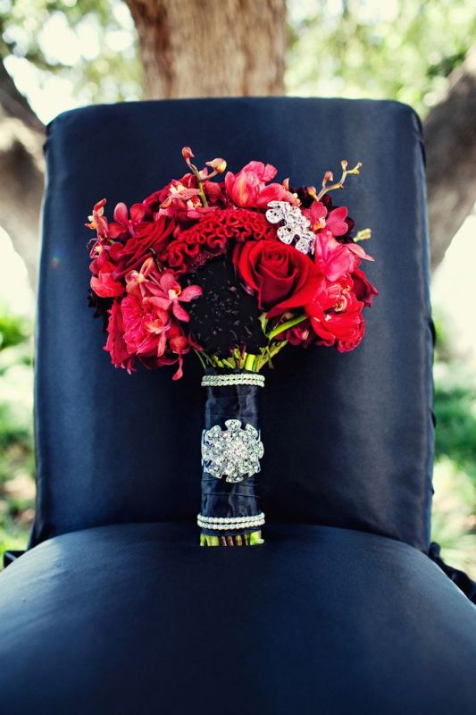 A bright red bridal bouquet with shiny touches and a navy wrap is a bold and contrasting idea