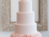 a large blush wedding cake with plain tiers and pink ruffles on top and on the bottom tier is a lovely idea for a romantic and glam wedding
