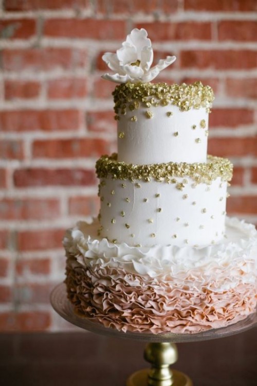 a white textural wedding cake with gold leaf and an ombre ruffle tier plus a white sugar bloom on top