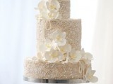 a beautiful white wedding cake fully covered with pearls and beads and with large white sugar blooms for a quirky wedding
