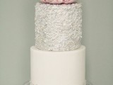 a white and silver wedding cake with a plain and polka dot tier, embellishments, lace and an oversized pink bloom