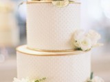 a white polka dot wedding cake with gold edge and fresh white blooms and leaves is very elegant