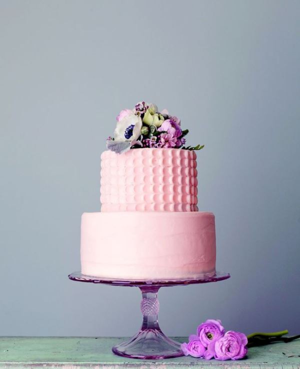 A light pink wedding cake with a textural patterned and a sleek tier plus fresh blooms on top