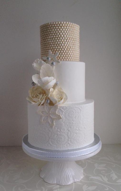 A refined wedding cake with a beaded and patterned lace tier, with sugar blooms and beads