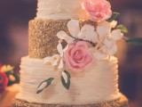 a white and gold textural wedding cake with glitter and ruffles, with sugar blooms and leaves