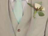 a tan three-piece wedding suit with a white flower boutonniere and a mint tie for a bright spring or summer wedding