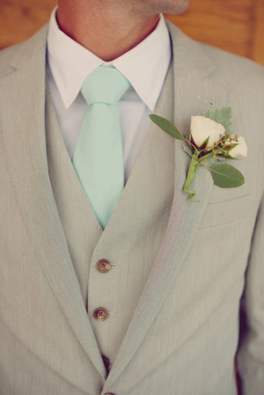 A tan three piece wedding suit with a white flower boutonniere and a mint tie for a bright spring or summer wedding