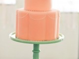 a coral wedding cake with white sugar detailing, a large white bloom and a mint colored stand for a colored wedding