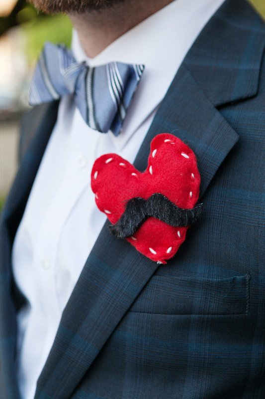 a fun and bold red fabric heart with a moustache boutonniere, which symbolizes the groom and adds a bit of fun to his look