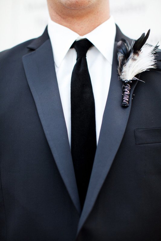 a feather wedding boutonniere with a black wrap will match a boho or Halloween groom style highlighting the time