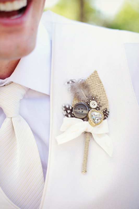 a beautiful wedding boutonniere of burlap, buttons, a heart rhinestone, feathers and a bow is a cool idea to make the groom's look bolder and catchier
