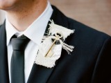 an unusual wedding boutonniere with white burlap, some printed fabric and a button and a large key shows off something personal for the groom