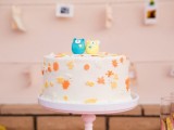 a white buttercream cake with yellow and orange leaves attached and a yellow and a blue little bear cake topper is a lovely and super cute idea
