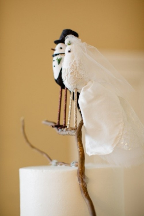 a white buttercream wedding cake with unique bird cake toppers that are dressed up as a marrying couple is wow