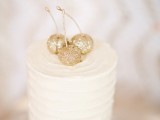 a white buttercream wedding cake topped with gold glitter cherries looks delicious and very cool, any simple wedding cake can be spruced up like that